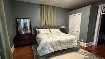Un dormitorio con cama, mesita de noche, lámpara, espejo y puerta.