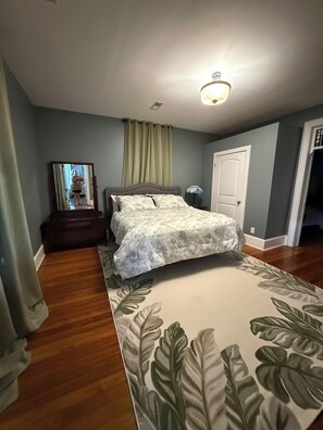 A bedroom with a bed, a nightstand, a lamp, a mirror, and a door. - 2nd Street Retreat (Pulaski)