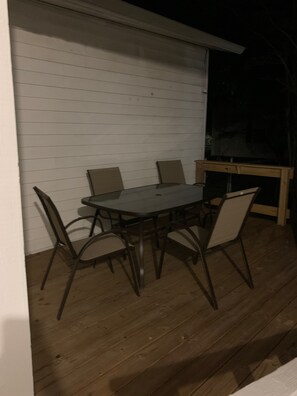 A wooden deck with a table and chairs, a small wooden table, and a white wall.