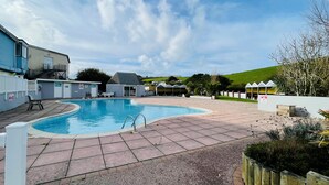 Ein Schwimmbecken mit geschwungener Form, umgeben von einer gepflasterten Terrasse mit weißem Zaun.