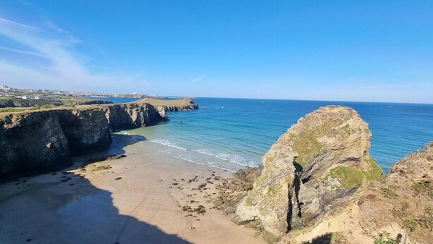 Eine Küstenlandschaft mit Klippen, einem Sandstrand und blauem Himmel.