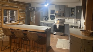 Eine kompakte Küche mit einer zentralen Kochinsel, Barhocker, Kühlschrank, Mikrowelle, Backofen und Spüle.