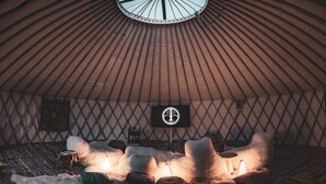 A yurt interior with a central seating area, a small table, and a wall-mounted screen. - Zen Jungle Retreat (Holsworthy)