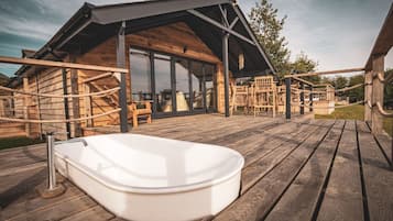 A wooden deck with a hot tub, a wooden cabin with large windows, and a rope ladder.