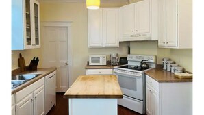 Una cocina con armarios blancos, encimera de madera, microondas, estufa y una lámpara colgante.