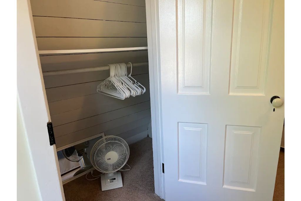 Un couloir avec une porte blanche, un ventilateur blanc et une étagère avec des cintres blancs.