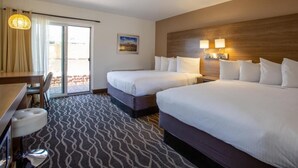 Ein Hotelzimmer mit zwei Betten, einem Schreibtisch mit Stuhl, einem kleinen Tisch und einem gemusterten Teppich.