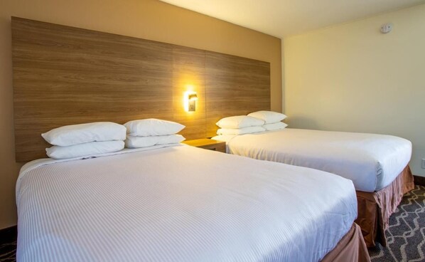 A hotel room with two beds, each with white linens and pillows, a wooden headboard, and a wall-mounted light fixture.