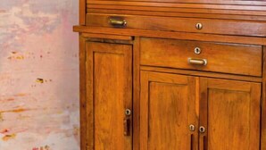 Ein Holzschrank mit horizontalen Lamellen oben, zwei Schubladen mit Griffen und zwei Türen mit Griffen.