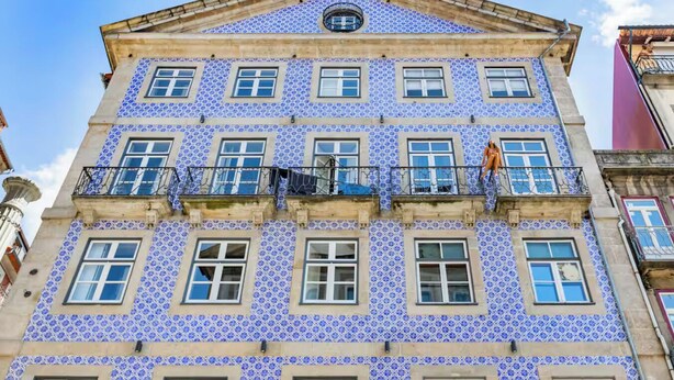 Ein Gebäude mit einer symmetrischen Fassade, zahlreichen Fenstern und einem zentralen Balkon mit einer Statue.