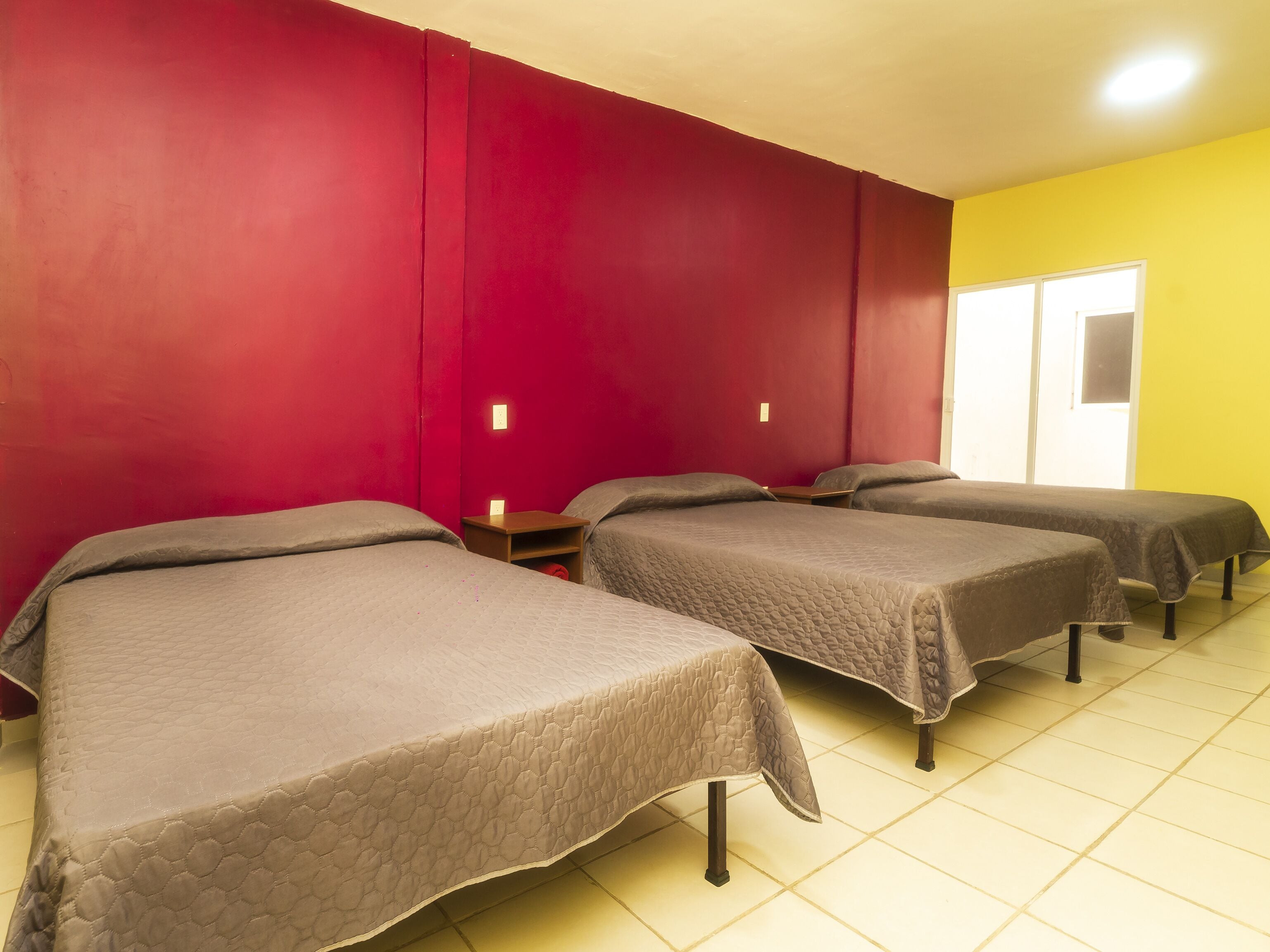 Une chambre d’hôtel avec trois lits, des murs rouges et un mur jaune.