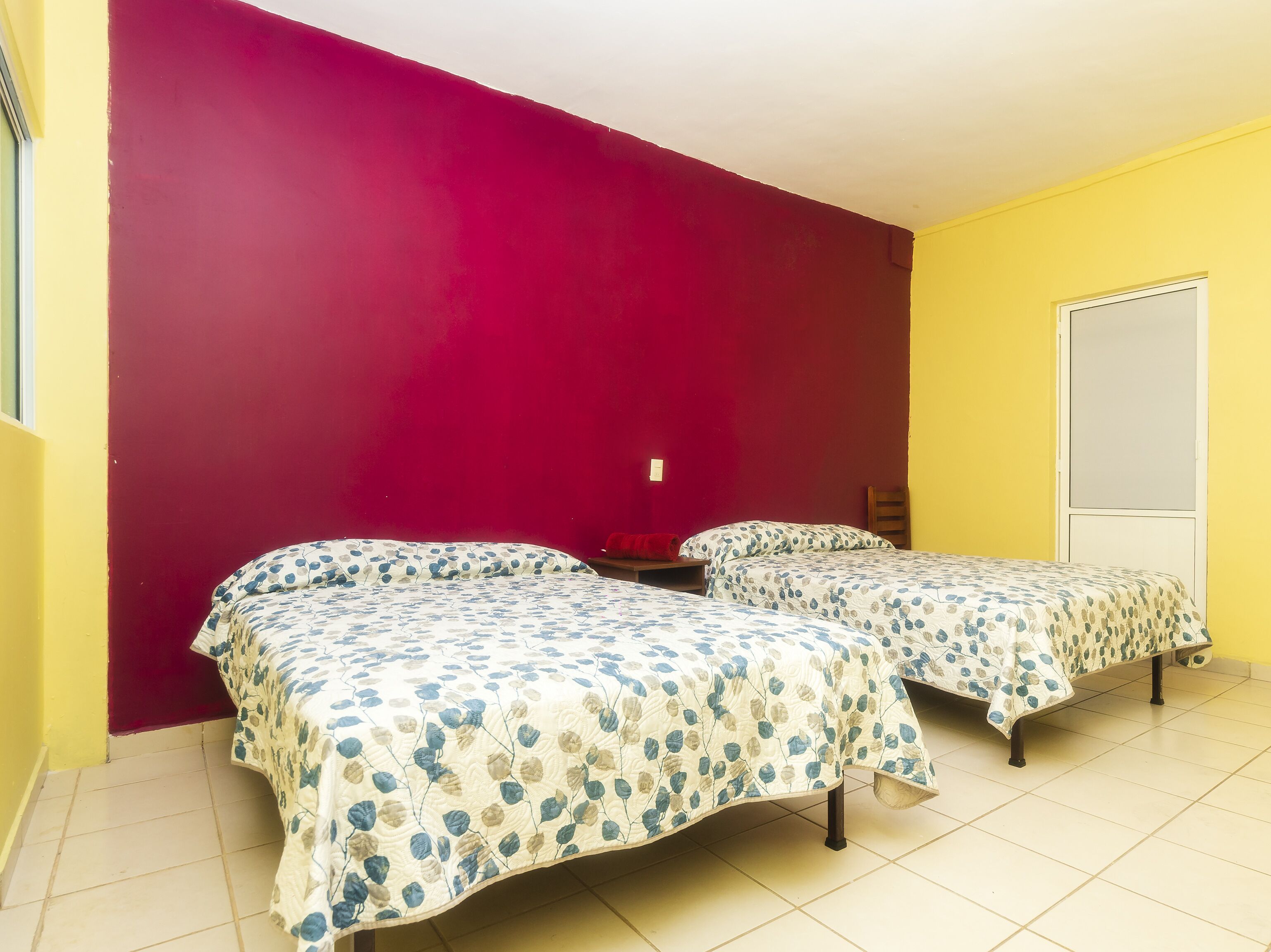 Une chambre avec deux lits, un mur rouge et un mur jaune.