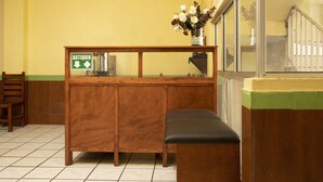 Um balcão de atendimento com uma placa indicando uma cabine, um banco e um vaso com flores.
