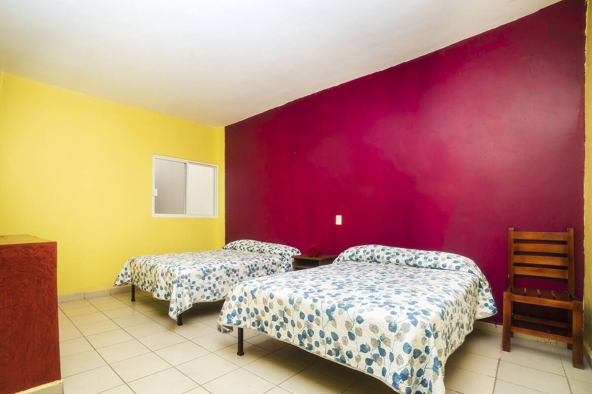 A room with two single beds, a wooden chair, a small table, and a window.