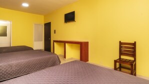 Quarto com duas camas, uma escrivaninha de madeira, uma cadeira, uma televisão e uma porta.