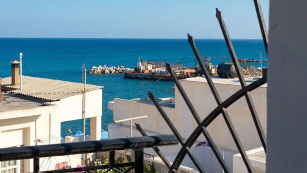 Vista costera con cielo despejado, un muelle y edificios al frente.