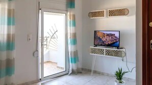 Una habitación con puerta de vidrio corrediza, un televisor sobre un pedestal y una planta en maceta.