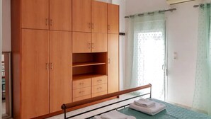 Un dormitorio con un armario de madera, una cama con edredón verde y una ventana con cortina.