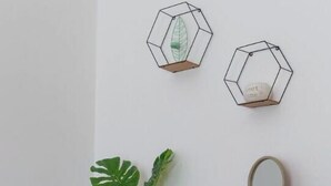 Un aparador de madera con dos cajones, un florero blanco con hojas verdes, un pequeño florero azul verdoso con flores blancas y un espejo redondo.