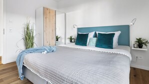 Ein modernes Schlafzimmer mit einem großen Bett, einem Holzschrank und einer kleinen Ablage mit Pflanzen.