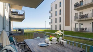 Ein Balkon mit Esstisch, der auf eine Wiese und ein Gebäude mit mehreren Balkonen blickt.