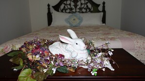 Una cama con una colcha estampada con motivos florales, un cabecero decorativo y una mesita de noche con una figurita de conejo blanco rodeada de flores.