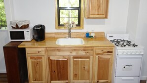 Una cocina con armarios de madera, un microondas blanco, una cafetera, un lavamanos y una estufa a gas.