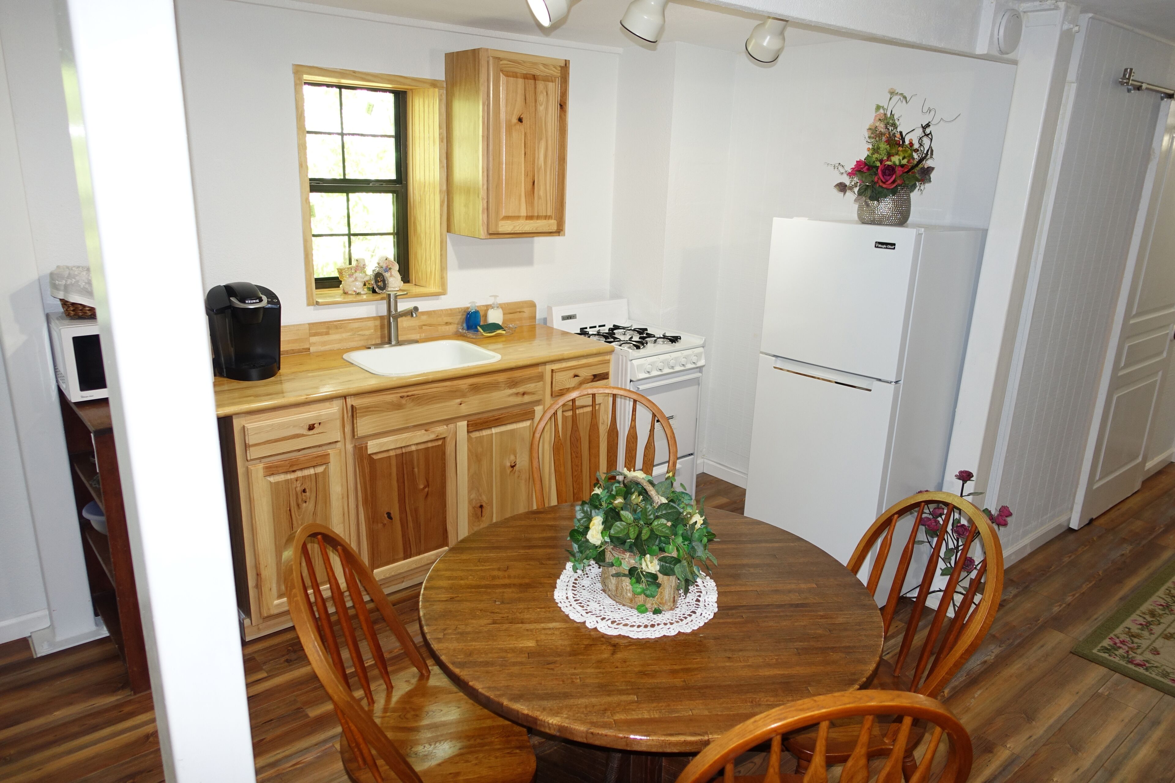 Une cuisine compacte avec des meubles en bois, une table de salle à manger ronde entourée de chaises, un réfrigérateur blanc et une cuisinière à gaz.