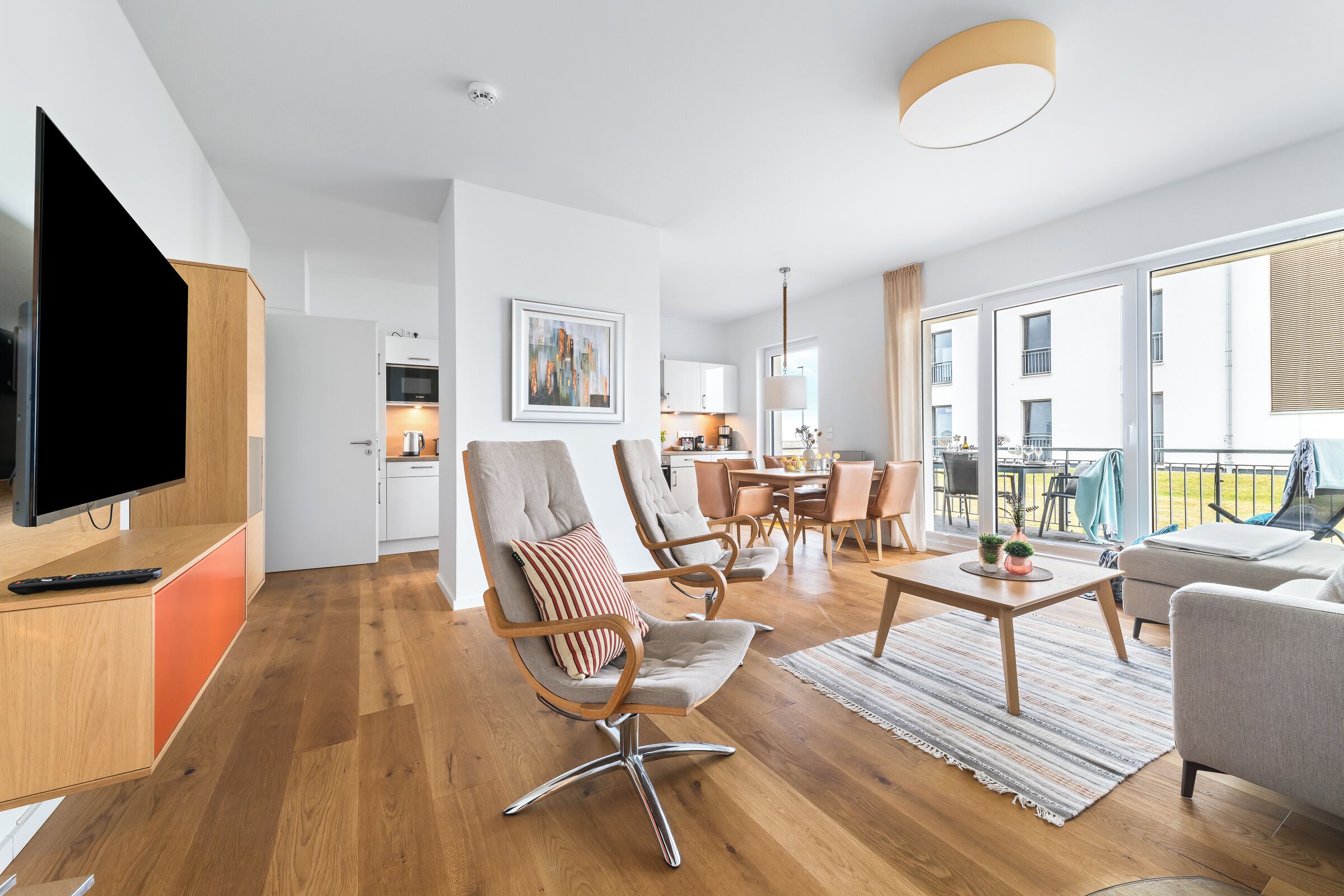 A modern living room with a flat-screen TV, wooden flooring, and a dining area with a table and chairs.