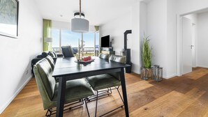 Een moderne eethoek met een zwarte tafel en groene stoelen, een groot raam met uitzicht, en een flatscreen televisie op de achtergrond.