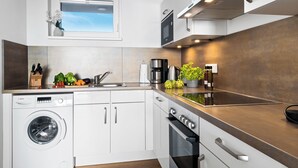 Una cocina moderna con lavadora integrada, horno y estufa. Incluye una ventana con vistas, un lavamanos y diversos electrodomésticos de cocina.