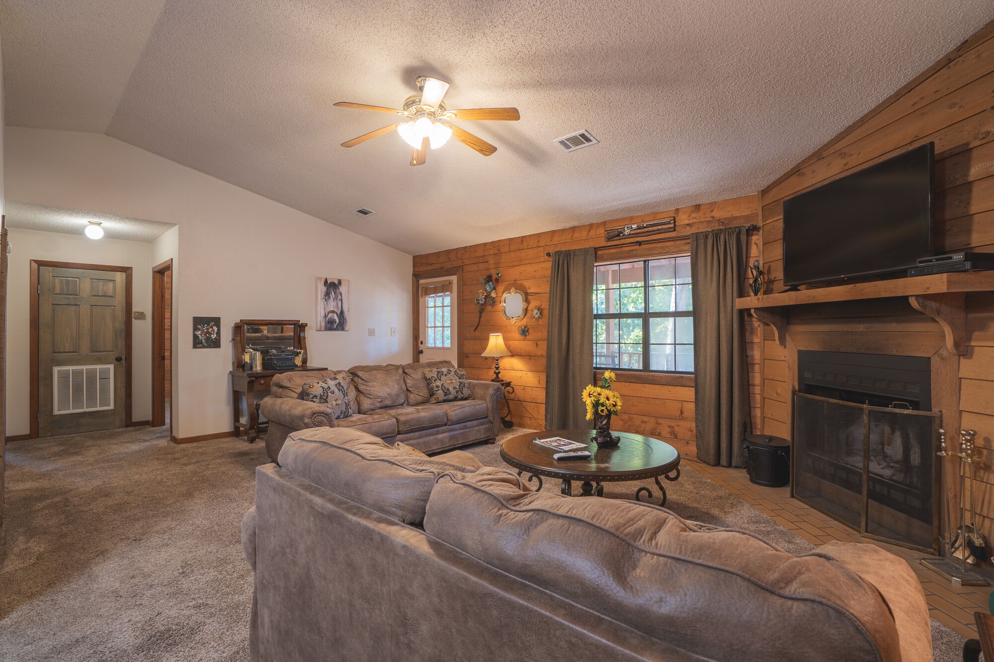 A cozy living room with a sectional sofa, a fireplace, a television, and a ceiling fan.