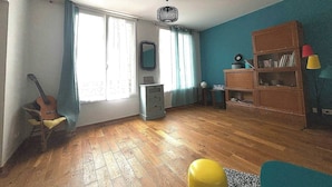 Una habitación con piso de madera, una guitarra, un tocador, un espejo y una estantería.