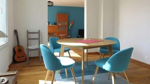 Una habitación con una mesa redonda y cuatro sillas azules, una guitarra y una estantería al fondo.