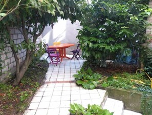 Relax in a serene, tree-shaded patio surrounded by lush greenery and a brick wall.