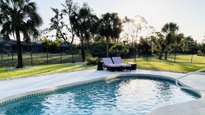 A swimming pool with a curved edge, surrounded by a paved deck. There are lounge chairs and a small table near the pool. - Luxury Retreat/Heated Pool/2Kings /n.Beach/Office (Rotonda West)