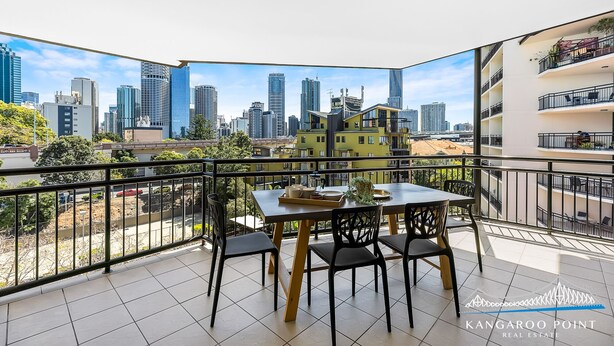 Een balkon met uitzicht op de stad, een tafel met stoelen en een leuning.