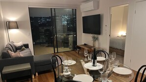 Een moderne eetruimte met een glazen tafel, zwarte stoelen en een stadsgezicht door grote ramen.