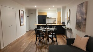 Een moderne woonkamer met een donkere bank en een eethoek met een houten tafel en stoelen.