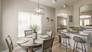 A modern kitchen with a central island, a dining area with a round table and chairs, and a living area with a sofa and coffee table. - Gilbert Luxury Remodel ~ EV Charger, 1-Level Comfort, Family & Pet-Friendly (Gilbert)