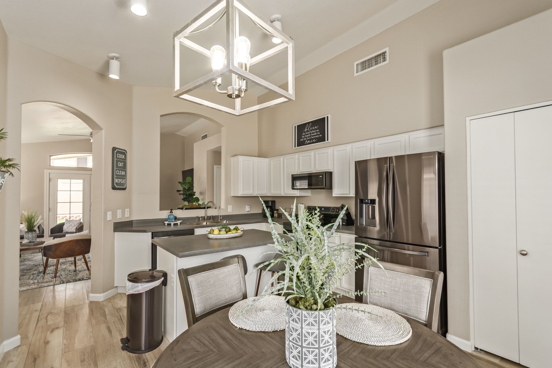 A modern kitchen with stainless steel appliances, a dining area with a wooden table and chairs, and a decorative plant centerpiece.