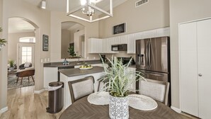 A modern kitchen with stainless steel appliances, a dining area with a wooden table and chairs, and a decorative plant centerpiece. - Gilbert Luxury Remodel ~ EV Charger, 1-Level Comfort, Family & Pet-Friendly (Gilbert)