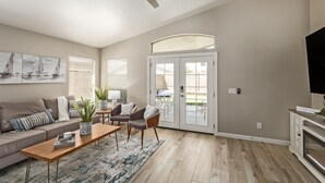 A spacious living room with a sofa, coffee table, and chairs, a ceiling fan, and a door leading to an outdoor area. - Gilbert Luxury Remodel ~ EV Charger, 1-Level Comfort, Family & Pet-Friendly (Gilbert)