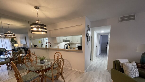 A modern kitchen with white cabinets, a dining area with a glass table and wooden chairs, and a living room with a green sofa. - Centrally located Condo, Sarasota Fl 34232 (Sarasota)