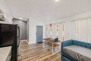 A compact living space with a kitchenette, a blue sofa, a dining table with a laptop, and a door leading to another room. - Private 1-bedroom unit for up to 3 guests with shared pool access, fast Wi-Fi, and a pet-friendly setup. (Orlando)