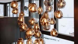 Un intérieur moderne agrémenté d’un luminaire sphérique original suspendu au plafond, de grandes fenêtres offrant une vue sur un paysage enneigé et d’un plancher en bois.