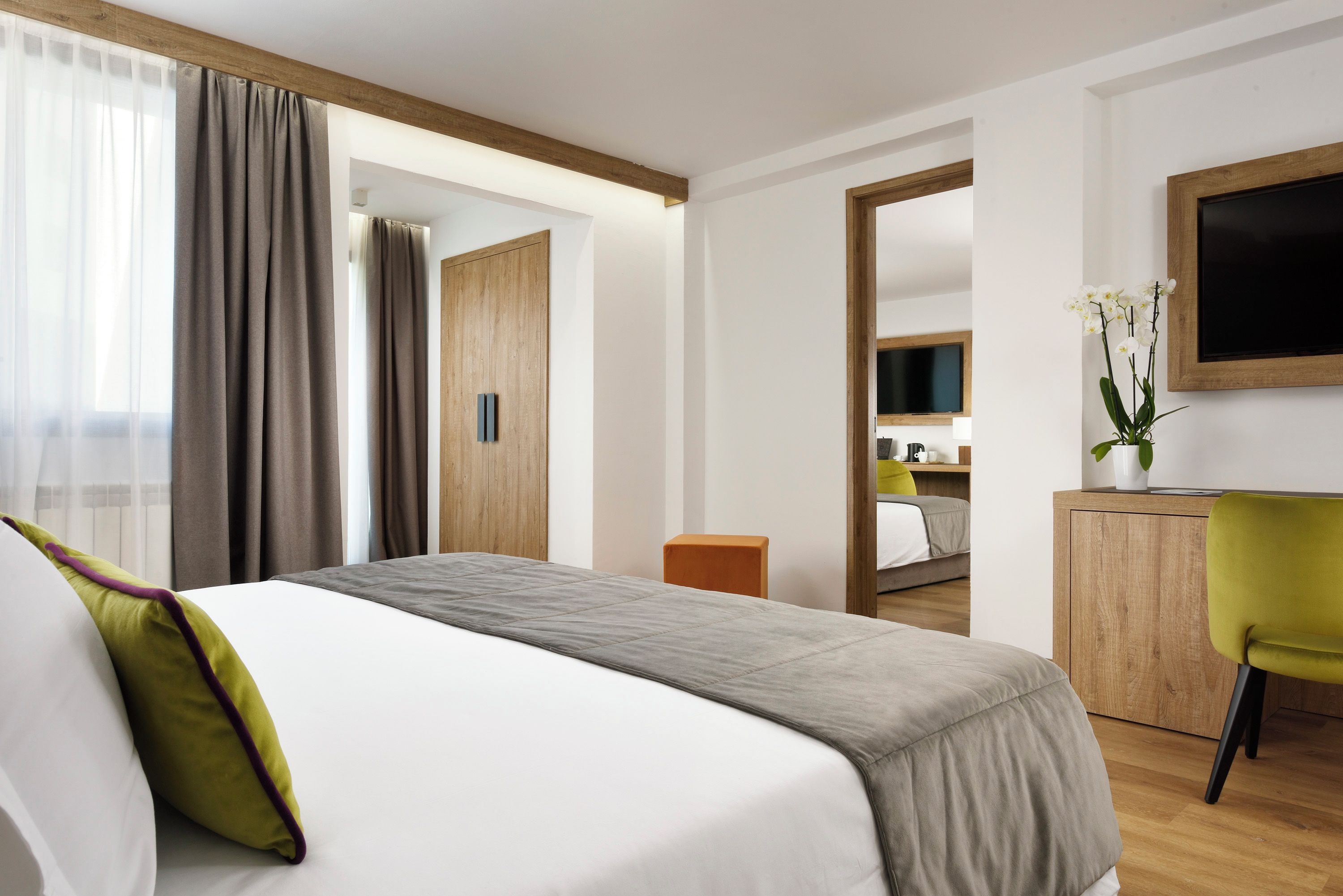 A hotel room with a bed, a desk, a chair, a TV, and a bathroom visible through an open door.