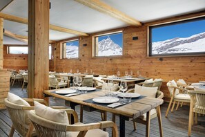 A wooden interior with tables set for dining, featuring mountain views through large windows. - Valtur Cervinia Cristallo Ski Resort (Valtournenche)