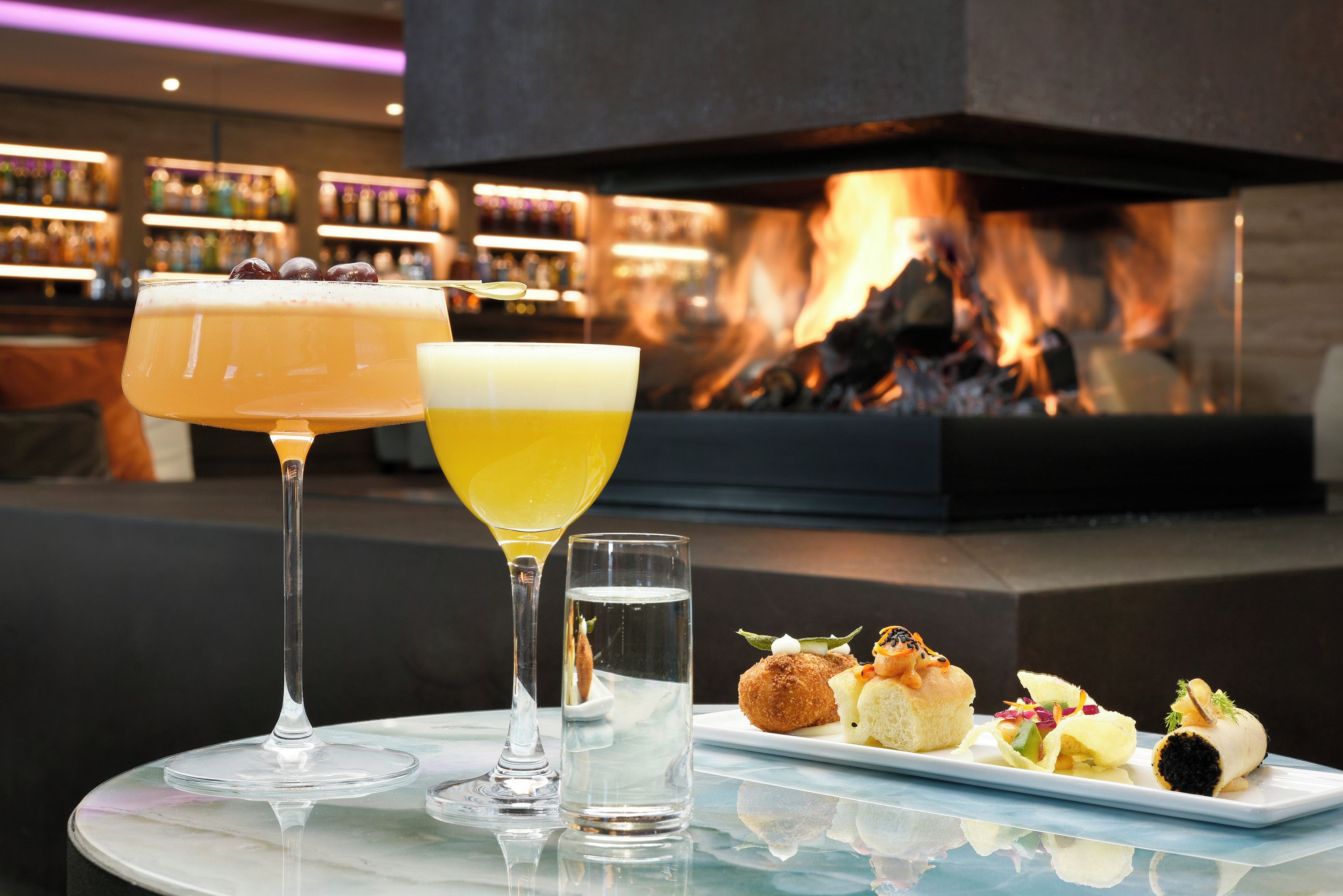 A table with a glass of cocktail, a glass of water, and a plate of appetizers.