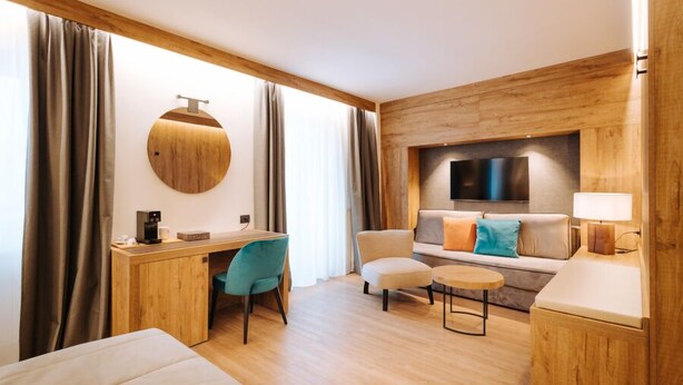 Une chambre d’hôtel moderne avec un bureau en bois, un canapé confortable, une petite table ronde et un téléviseur fixé au mur.